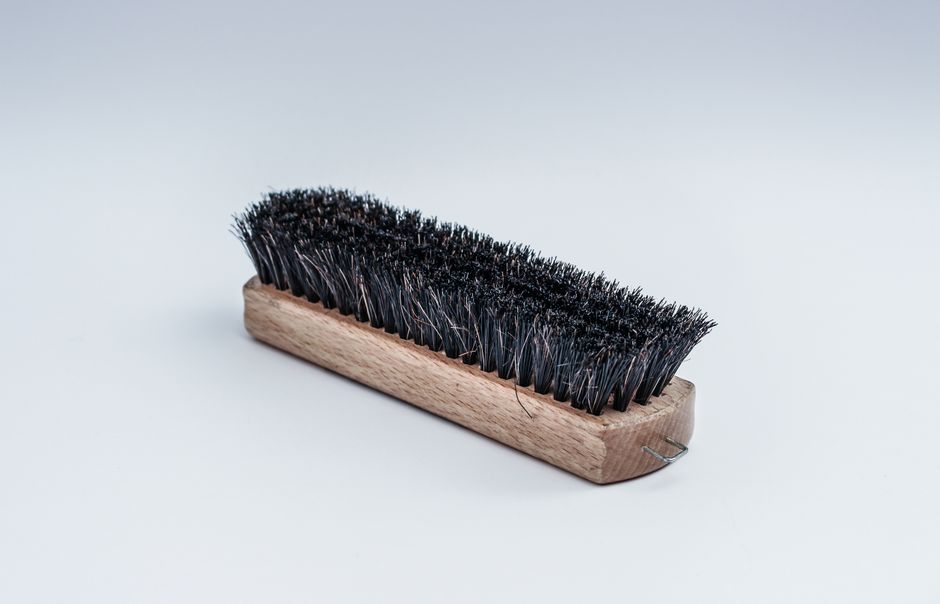 Close-up of a wooden cleaning brush with dense black bristles on a white background.