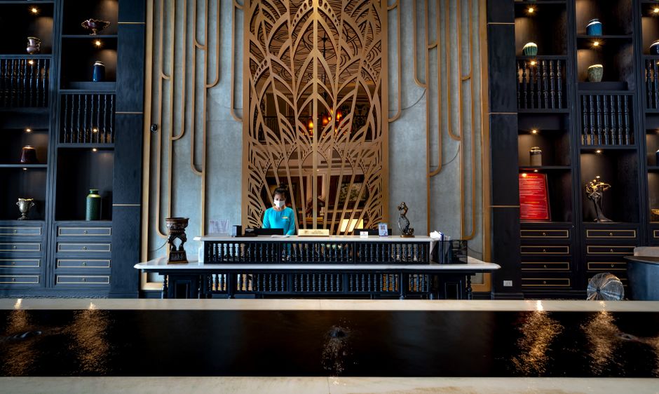 Elegant hotel reception with a modern design, featuring a receptionist at the front desk, ornate decor, and luxury ambiance.